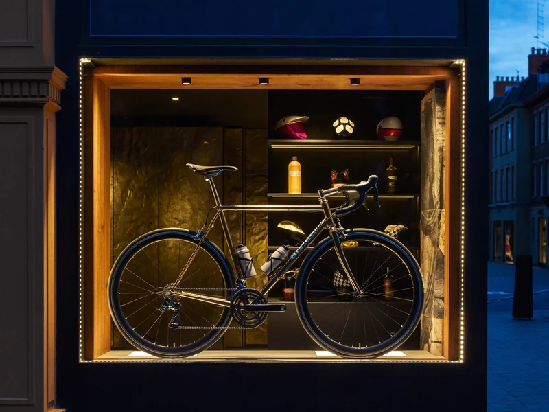 Illustrierte Schaufensterszene in der Dämmerung mit einem Rennrad und dunklen Zubehörregalen